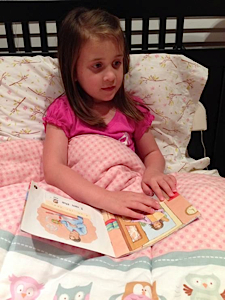 little girl reading braille in bed