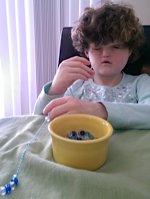 A young girl strings beads at a table