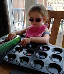 Ellie playing with buttons in a muffin tin