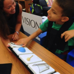 Ivan exploring the tangible calendar on the desk while his teacher watches