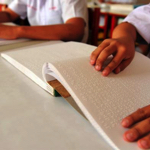 Students' hands reading braille books on a desk