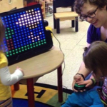 Kids in a preschool classroom gathered around the LightAide device