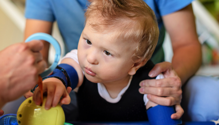 A visually impaired baby boy in PT reaches for a toy.