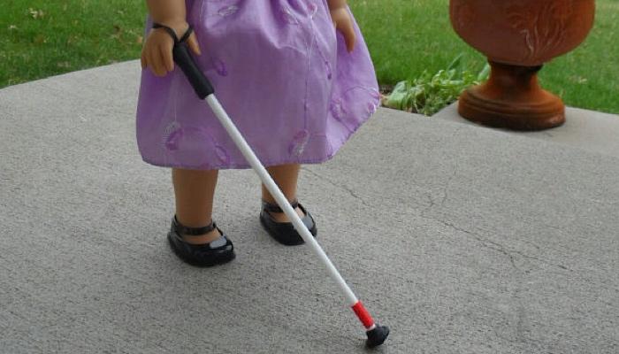 American Girl doll holding a white cane