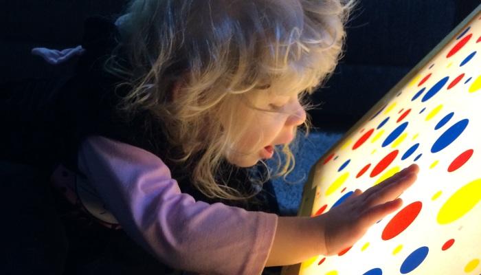 A little girl with her hand on a light board with colorful shapes