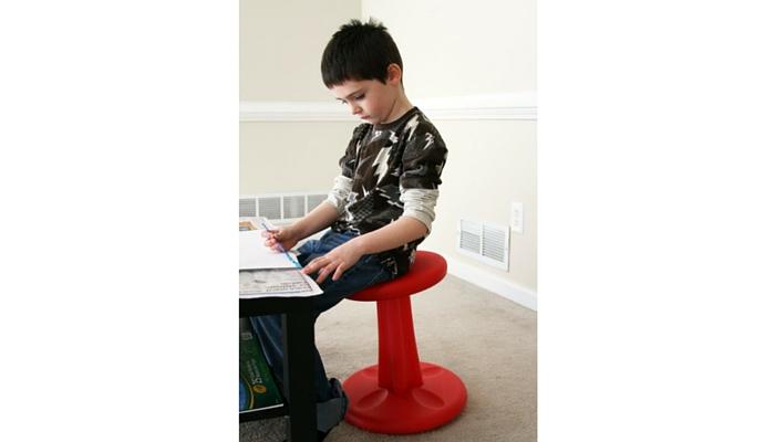 child sitting on red wobble chair at desk