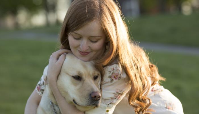 A young woman with red hair hugging her guide dog, a yellow lab