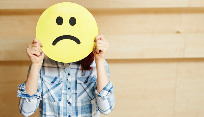 woman holding a sad face mask in front of her face