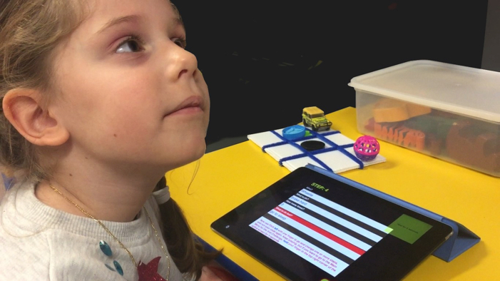 young girl listening to the Ballyland coding app, with a tactile game grid at hand