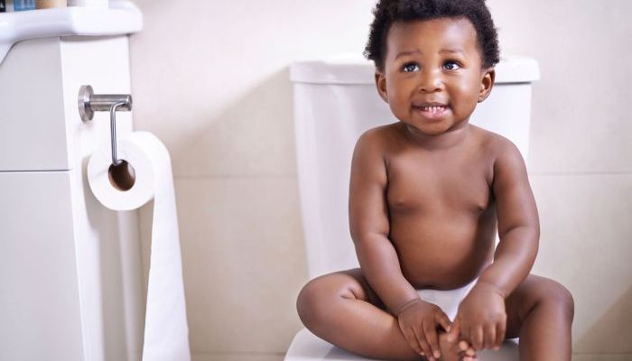 Adorable baby boy sitting on the toilet in the bathroom.