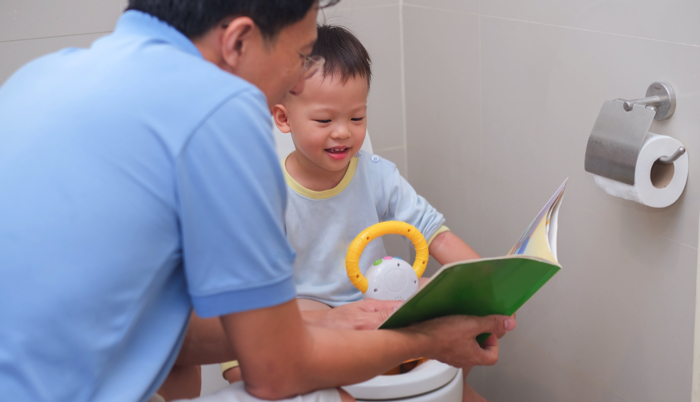 little boy reading a book with his dad while sitting on the potty