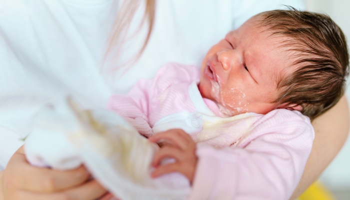 Mother holding a spitting up newborn.