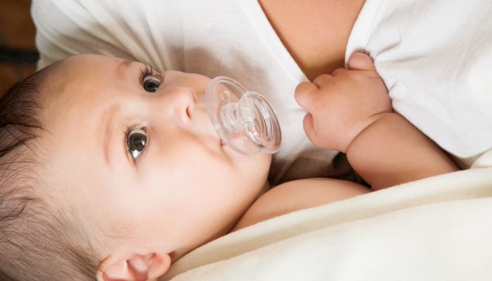 Baby with pacifier resting in its mother's arms.