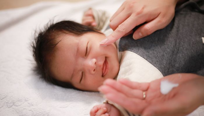 Parent moisturizing baby's face.