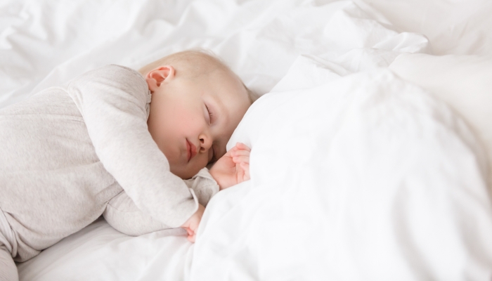 Baby sleeping with open arms and without pacifier in a cradle.