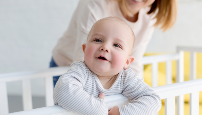 Baby smiling with her mother behind a baby crib.