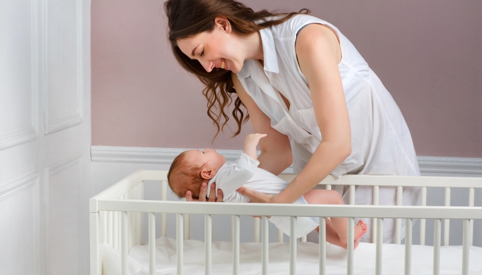 Beautiful mother smiling with her 3-month-old baby placed in the baby's crib.