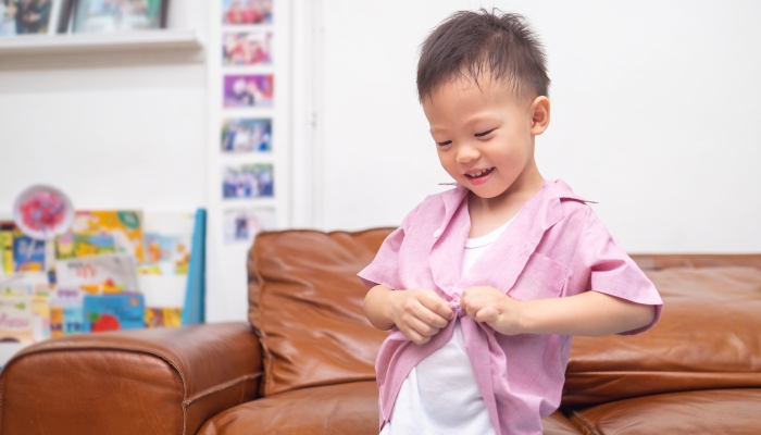 Cute little Asian putting on shirt at home