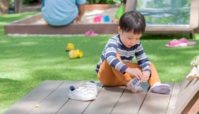 Cute little boy taking off his sock at the park