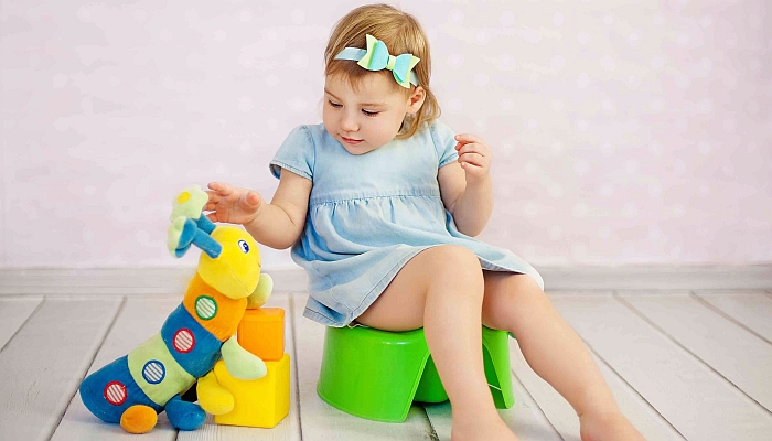 Cute little girl potty training with a toy at house.
