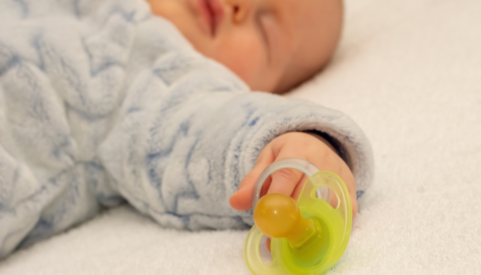 Little baby boy is peacefully sleeping and holding a pacifier dummy in his hand.