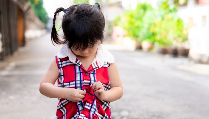 Little girl tries to button her clothes by herself.