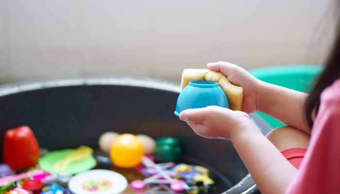 Mother cleaning colorful plastic bath toys in water basin.