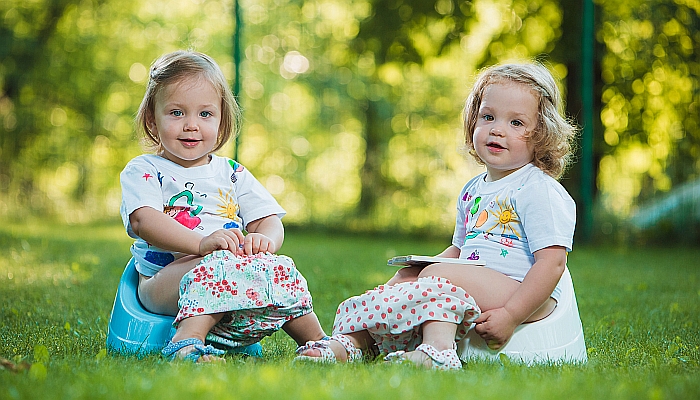 The two little baby girls sitting on pottys against green grass.