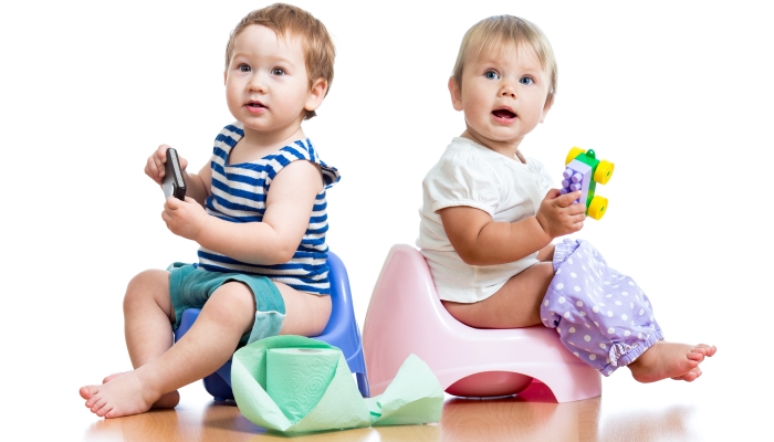 Toddlers sitting on chamber pot and playing with toys.