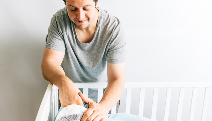 Young adult man preparing the mattress and sheets for his son's bassinet.