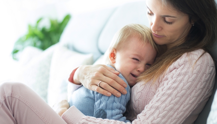 Young mother holding her crying toddler boy.