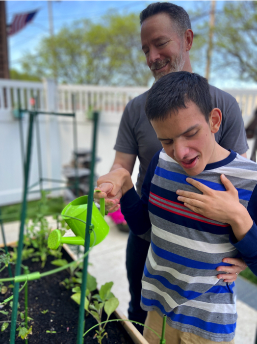 Ivan and his dad watering plants in a raised garden bed.