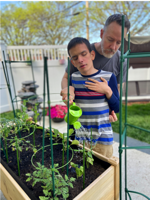 Ivan and his dad watering plants in a raised garden bed.