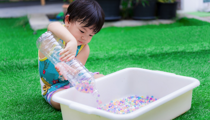 A little boy outside playing with water beads.