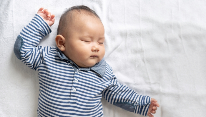 A baby boy in a striped shirt is sleeping in bed.