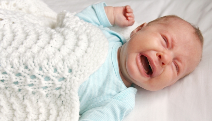 A cute one month old newborn baby is crying in the crib.