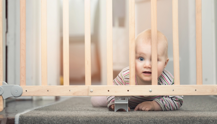 Baby behind safety gates in front of stairs at home.