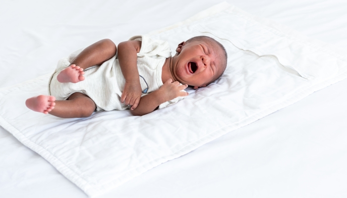 Baby newborn is crying on a white bed.