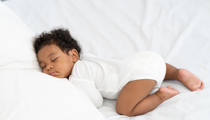 Black african american baby sleeping on a white mattress.