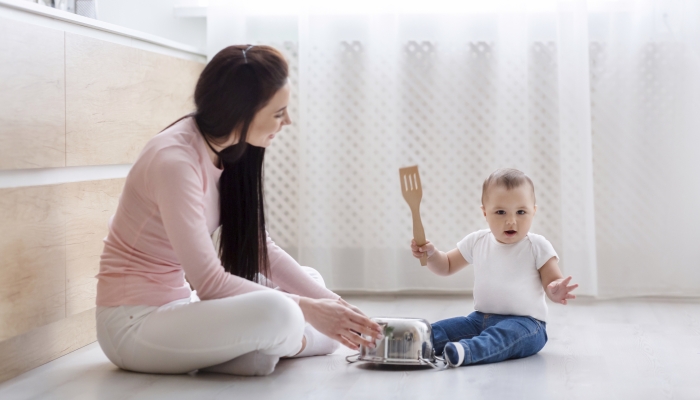 Little boy drumming on metal saucepan, sitting with mom.