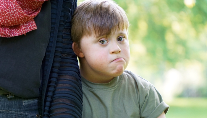 Little boy with down syndrome cuddles up to his mother and looks a bit sad.