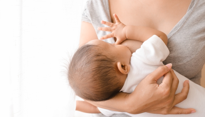 Mother breastfeeding her newborn baby beside window.