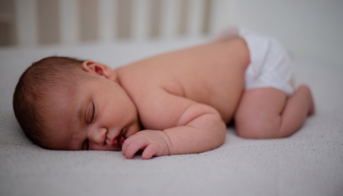 Newborn baby girl sleeping face down in her white cradle.