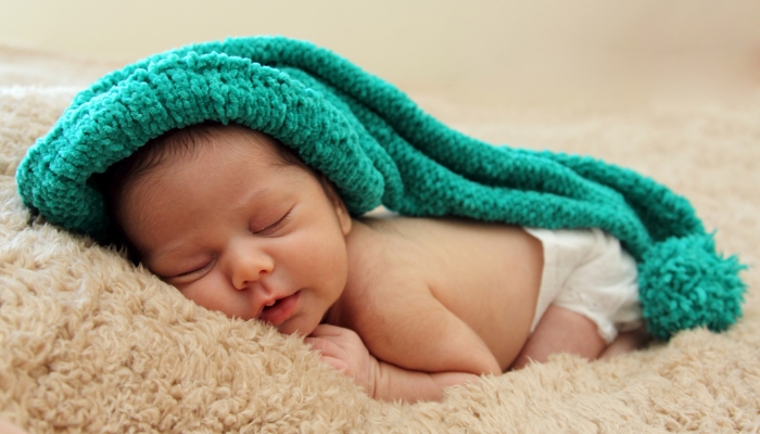 Newborn baby is wearing a blue hat and laying down sleeping.