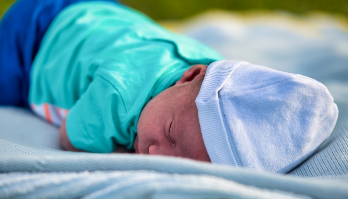 Newborn baby lying down sleeping outdoor in the city park at sunset.