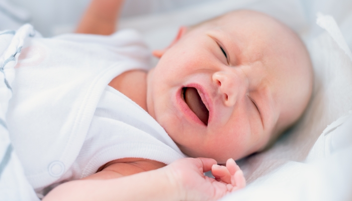 The newborn is crying while lying in the crib.