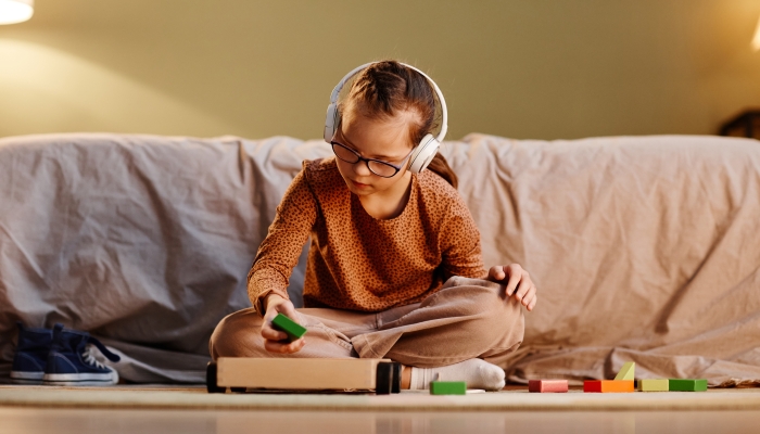 Young girl with down syndrome playing with toy blocks alone and wearing noise cancelling earphone.
