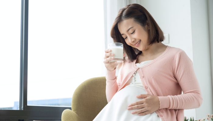 Young pregnant woman with glass of milk in the room.