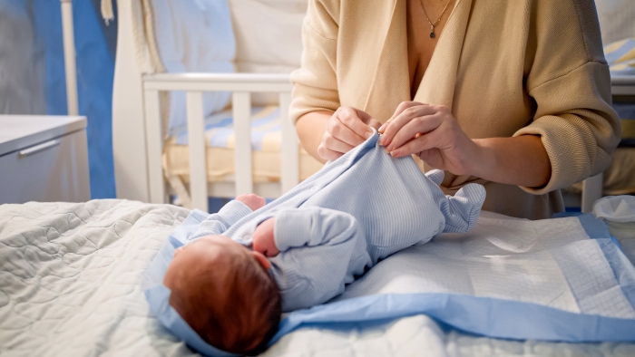 Young woman dressing her newborn baby boy in new clean and dry clothes.