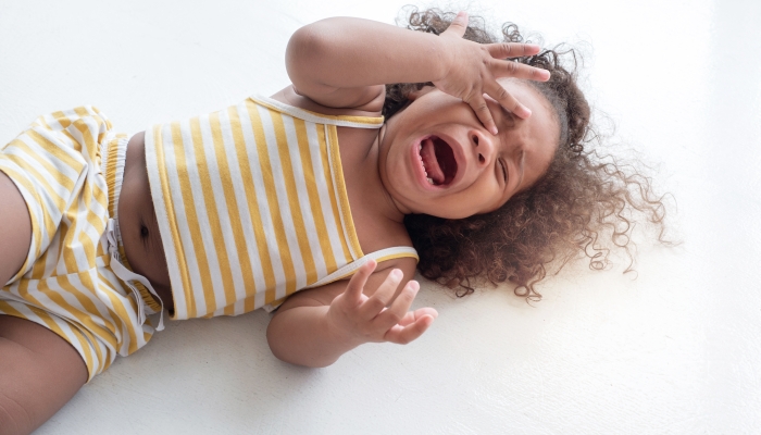 child girl crying and shouting with tantrum lying on the floor at home